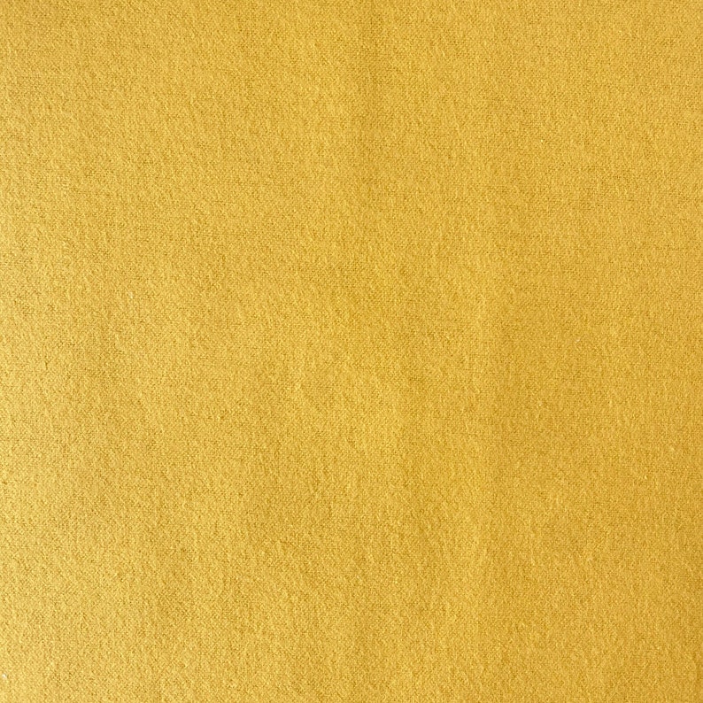 May include: Close-up of a solid, textured fabric in a warm, golden-yellow hue. The material has a slightly fuzzy appearance, suggesting a soft texture. The color is consistent across the entire surface, with subtle variations in tone.