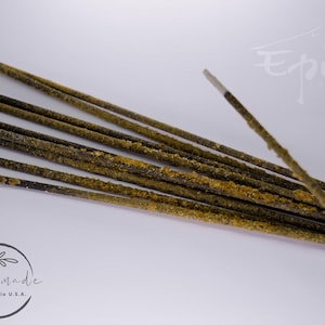 May include: A bundle of brown incense sticks with a light brown coating. The sticks are arranged in a fan shape on a white surface. The text "Handmade Akron, Ohio U.S.A." is visible in the lower left corner of the image.