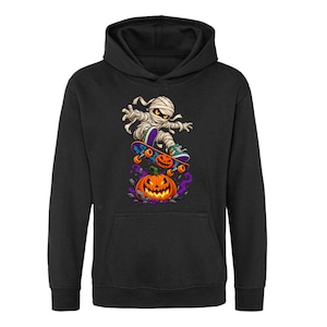 May include: A black hooded sweatshirt featuring a graphic print of a mummy on a skateboard jumping over a glowing orange jack-o'-lantern. The mummy wears teal and purple trainers, and the skateboard has a jack-o'-lantern design on the deck.
