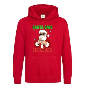 May include: A red hooded sweatshirt featuring a graphic of Santa Claus wearing sunglasses and making a hand gesture. The text "SANTA SAYS" is above the Santa graphic, and "SIX SEVEN" is below.