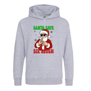 May include: A light gray hoodie featuring a graphic of Santa Claus wearing sunglasses and making a hand gesture. The text "SANTA SAYS" is above the Santa graphic, and "SIX SEVEN" is below. The hoodie has a front pocket and a hood.