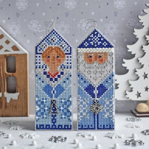 Può includere: Due ornamenti a punto croce blu e bianco che raffigurano una donna e un uomo in abiti invernali. La donna indossa un cappello e un cappotto blu con bordatura bianca. L'uomo indossa un cappello e un cappotto blu con barba bianca. Entrambi gli ornamenti hanno un ciondolo a fiocco di neve argentato.