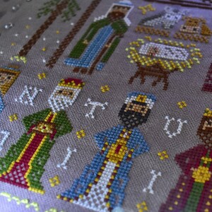 K&ouml;nnte beinhalten: Eine detaillierte Kreuzsticharbeit, die eine Weihnachtskrippe darstellt. Das Design zeigt Figuren der Heiligen Drei K&ouml;nige, das Jesuskind in einer Krippe und andere biblische Figuren. Die Farbpalette umfasst Schattierungen von Gr&uuml;n, Blau, Rot und Gold auf einem neutralen Hintergrund.