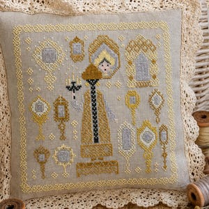 Puede incluir: Un coj&iacute;n cuadrado de lino beige con un dise&ntilde;o de punto de cruz que muestra una figura central sosteniendo una vela, rodeada de varios espejos ornamentados en oro y plata. El coj&iacute;n est&aacute; bordeado por un marco amarillo de punto de cruz y encaje crema.