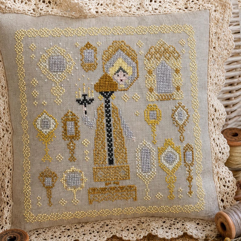 Puede incluir: Un coj&iacute;n cuadrado de lino beige con un dise&ntilde;o de punto de cruz que muestra una figura central sosteniendo una vela, rodeada de varios espejos ornamentados en oro y plata. El coj&iacute;n est&aacute; bordeado por un marco amarillo de punto de cruz y encaje crema.