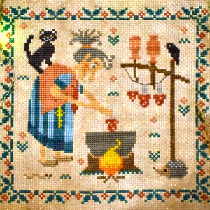 May include: A cross-stitch embroidery depicting a witch stirring a cauldron over a fire. The witch is wearing a red and blue dress and has a black cat on her shoulder. There are three birds perched on a wooden post in the background.