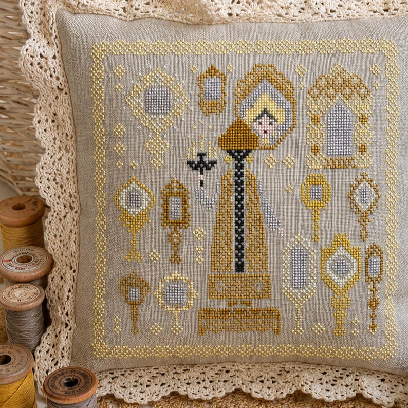 Puede incluir: Un coj&iacute;n cuadrado de lino con un dise&ntilde;o de punto de cruz en tonos dorados, amarillos y grises. El bordado muestra una figura central sosteniendo un candelabro rodeada de varios espejos de mano y marcos ornamentados, con borde de encaje.