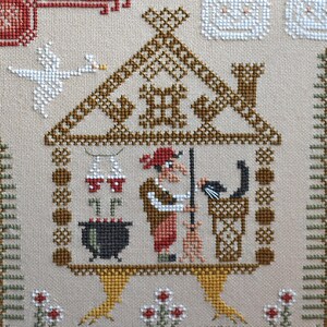 May include: Cross-stitch embroidery featuring a whimsical scene of a witch in a house with a black cat, cauldron, and broom. The design includes a white swan, red and white accents, and a detailed roof. The background is a neutral beige color.