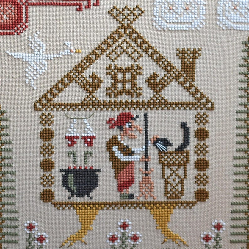 May include: Cross-stitch embroidery featuring a whimsical scene of a witch in a house with a black cat, cauldron, and broom. The design includes a white swan, red and white accents, and a detailed roof. The background is a neutral beige color.