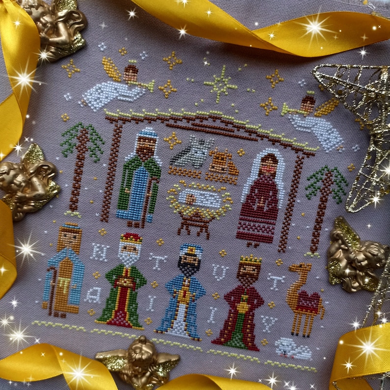 K&ouml;nnte beinhalten: Ein Kreuzstich, der die Weihnachtsgeschichte darstellt, mit Maria, Josef, dem Jesuskind, den Heiligen Drei K&ouml;nigen, Engeln und einem Kamel. Das Design verwendet Blau, Gr&uuml;n, Rot und Gold auf grauem Hintergrund. Das Wort "HAIL" ist gestickt.