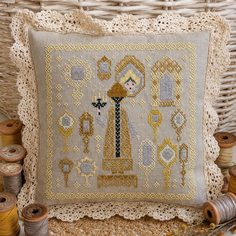 Puede incluir: Un coj&iacute;n cuadrado de lino beige con un dise&ntilde;o en punto de cruz de una figura central que sostiene un candelabro, rodeada de varios espejos de mano ornamentados en tonos dorados, plateados y negros, con un borde de encaje de ganchillo crema.