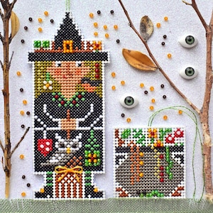 May include: Cross-stitch pattern of a witch holding a cat and a cauldron. The witch is wearing a black hat and dress with green accents. The cauldron is filled with green and red items. The background is white with brown branches and orange and brown beads.