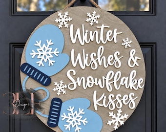 May include: A round wooden door sign featuring the white text Winter Wishes & Snowflake Kisses. The sign is decorated with two light blue mittens with dark blue cuffs and several white snowflake cutouts, all suspended by a twine rope.
