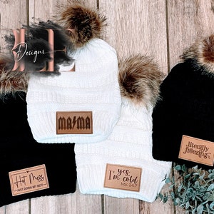 May include: Four winter beanies in black and white with faux fur pom-poms. Each beanie has a leather patch with text: "Hot Mess," "Mama," "I'm cold," and "literally freezing."