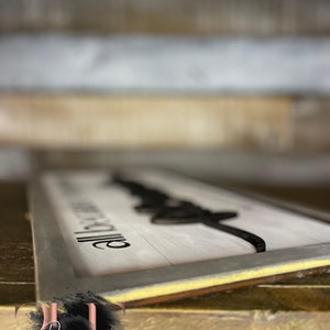May include: A rectangular wooden sign with a white background and black text and design. The sign reads "All because two people fell in love." The sign has a gray frame and is displayed on a wooden surface.