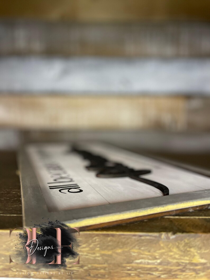 May include: A rectangular wooden sign with a white background and black text and design. The sign reads "All because two people fell in love." The sign has a gray frame and is displayed on a wooden surface.