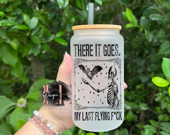 May include: Frosted glass tumbler with a bamboo lid and a reusable straw. The tumbler features a black graphic of a skeleton and bat with the text "THERE IT GOES, MY LAST FLYING F*CK".