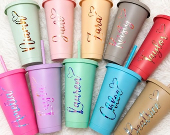Könnte beinhalten: Eine Sammlung von zehn bunten Bechern mit Deckeln und Strohhalmen. Jeder Becher hat eine andere Pastellfarbe und trägt einen Namen in Schreibschrift mit einem Herzdesign. Die Farben umfassen Rosa, Grün, Lila, Blau und Beige.