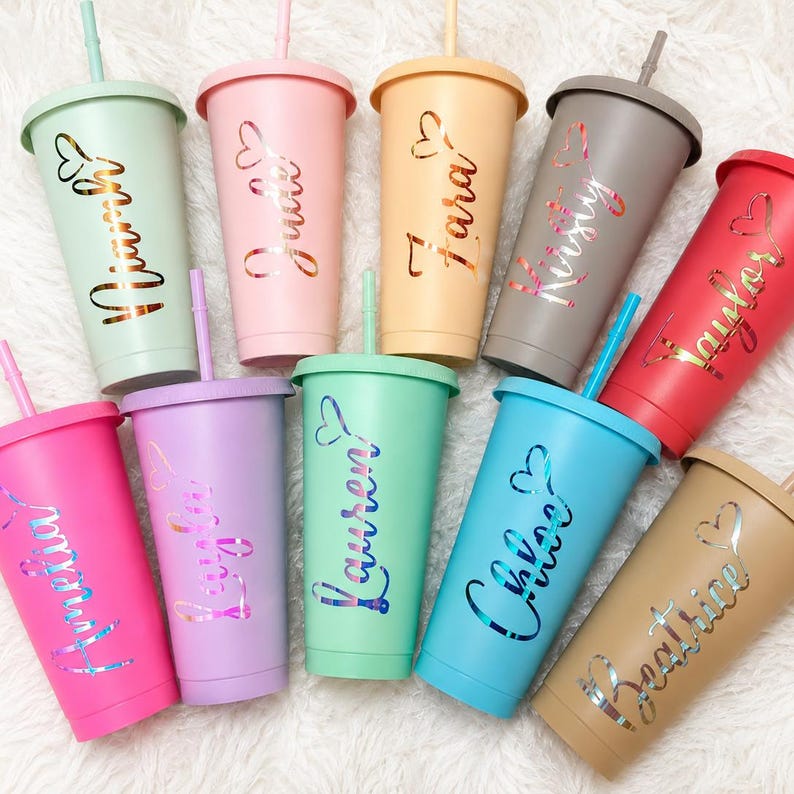 Puede incluir: Una colecci&oacute;n de diez vasos de colores pastel con tapas y pajitas. Cada vaso tiene un color pastel diferente y presenta un nombre en una fuente cursiva con un dise&ntilde;o de coraz&oacute;n. Los colores incluyen rosa, verde, morado, azul y beige.