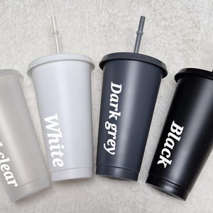 May include: Four reusable tumblers with lids and straws in frosted clear, white, dark grey, and black. Each tumbler has the colour name printed on the side.