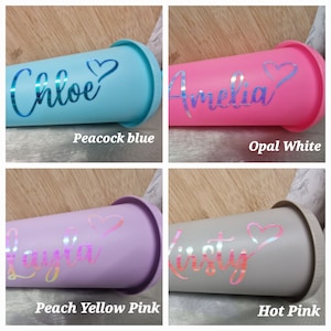 Puede incluir: Cuatro vasos personalizados en azul pavo real, blanco &oacute;palo, rosa melocot&oacute;n amarillo y rosa intenso. Cada vaso tiene un nombre y un gr&aacute;fico de coraz&oacute;n con acabado hologr&aacute;fico. Los nombres son Chloe, Amelia, Layla y Kirsty. El texto "Peacock blue", "Opal White", "Peach Yellow Pink" y "Hot Pink" est&aacute; debajo.