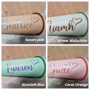 Puede incluir: Cuatro vasos en rosa atardecer, verde malaquita, azul jacinto y naranja coral. Cada vaso tiene un nombre y un coraz&oacute;n decorativo. Los nombres son Beatrice, Liamh, Lauren y Jude. Los vasos est&aacute;n sobre una superficie de madera.