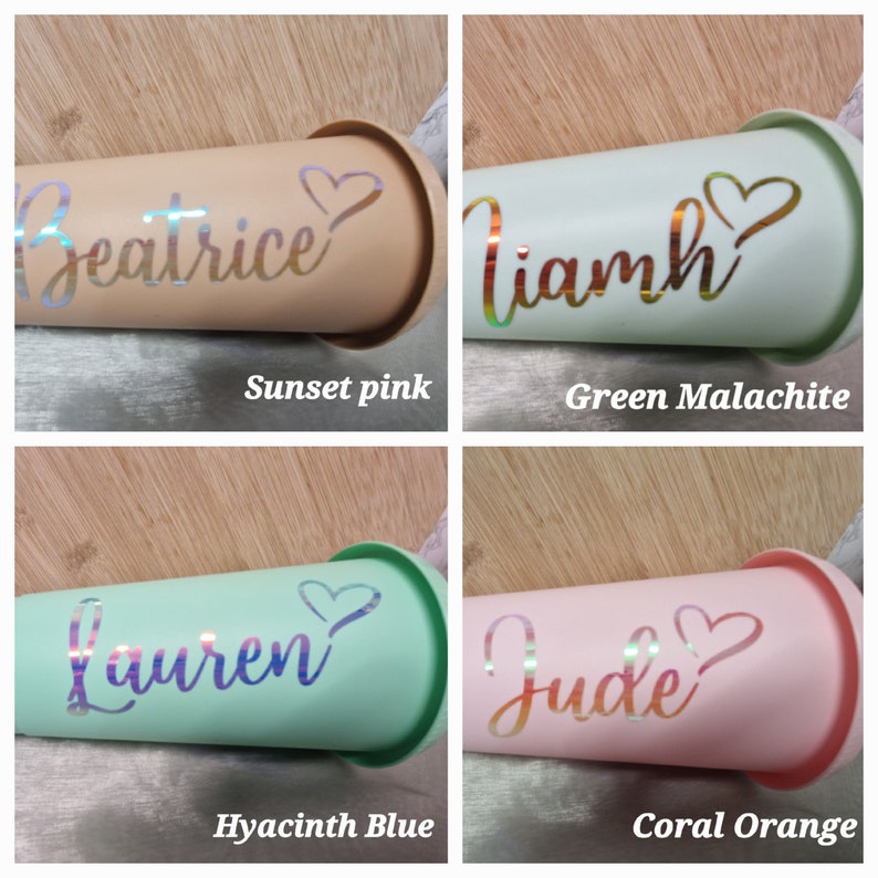 Puede incluir: Cuatro vasos en rosa atardecer, verde malaquita, azul jacinto y naranja coral. Cada vaso tiene un nombre y un coraz&oacute;n decorativo. Los nombres son Beatrice, Liamh, Lauren y Jude. Los vasos est&aacute;n sobre una superficie de madera.