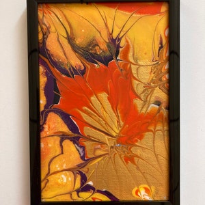May include: Abstract painting in a black frame with swirling patterns of yellow, orange, red, and purple paint.