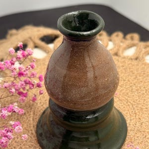 May include: A handcrafted ceramic vase with a dark green base and rim, and a brown, textured body. The vase has a bulbous shape and a narrow opening. The vase is likely used for decorative purposes or to hold flowers.