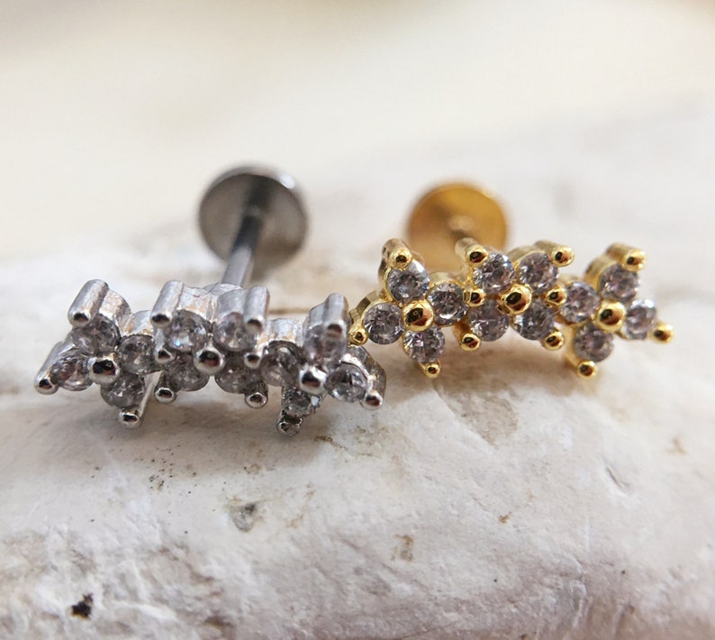 May include: Two silver and gold body jewelry pieces with a row of small clear stones. The jewelry is in the shape of a curved line.