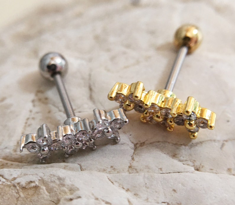 May include: Two barbell style body jewelry pieces with a clear crystal flower design. One is gold and the other is silver.