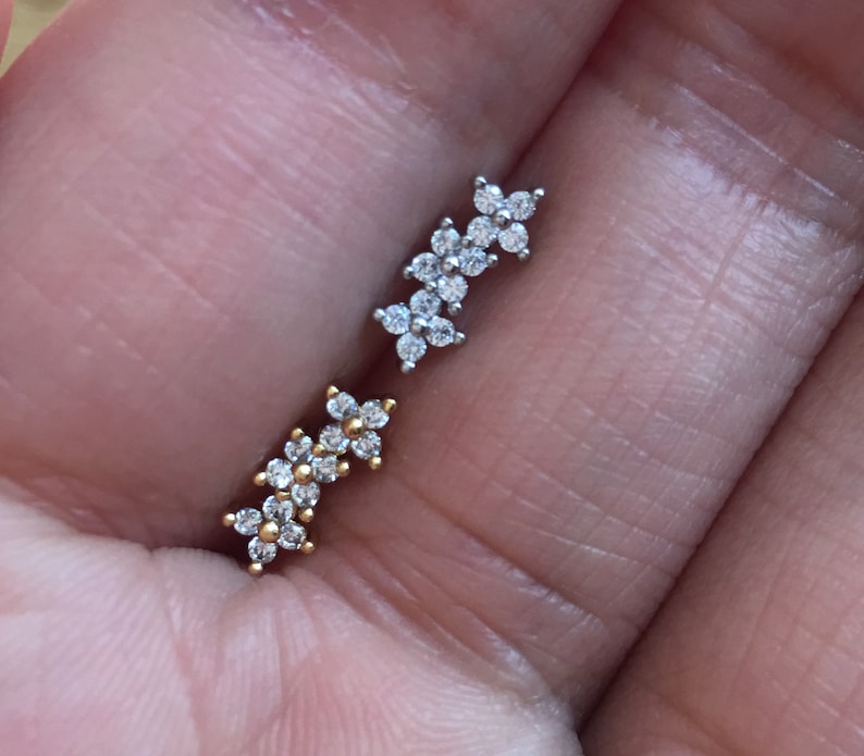 May include: Two pairs of small, silver and gold flower-shaped earrings with clear cubic zirconia stones.
