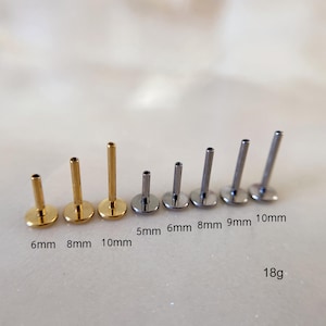 Op de afbeelding: Een assortiment platte labret studs in goud- en zilverkleuren. Maten variëren van 5 mm tot 10 mm, 18g. De studs hebben een platte schijfbasis en een rechte staaf voor piercings.