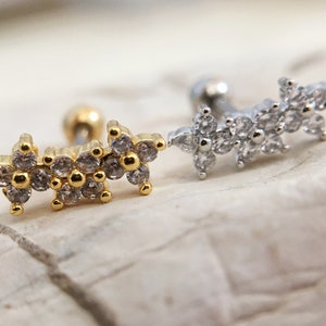 May include: Two gold and silver body jewelry pieces with a row of small, clear, sparkling stones in the shape of flowers.