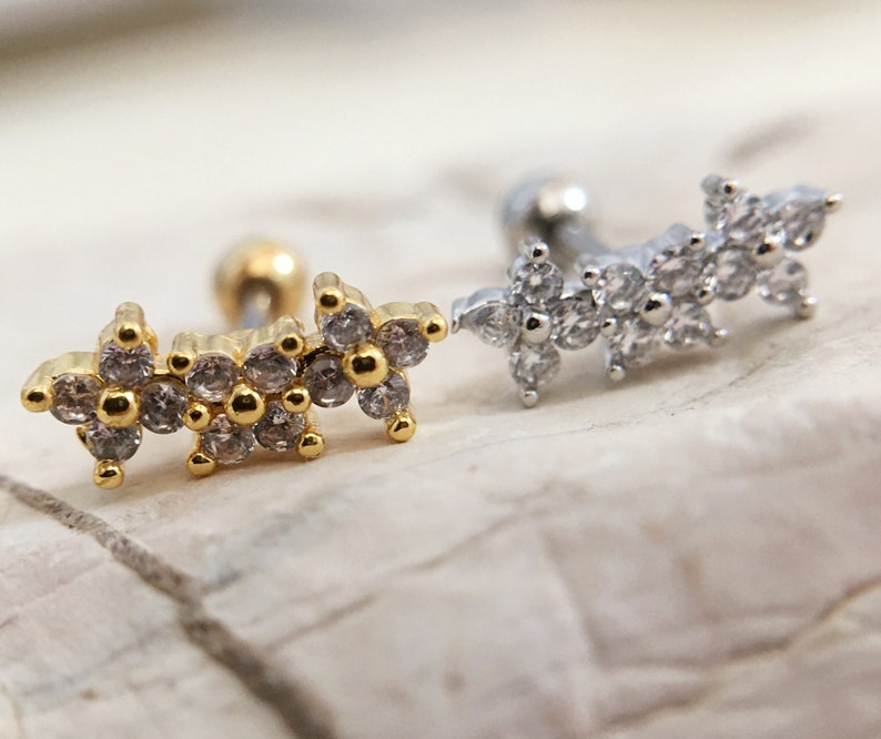 May include: Two gold and silver body jewelry pieces with a row of small, clear, sparkling stones in the shape of flowers.
