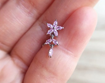 May include: A silver flower-shaped earring with pink cubic zirconia stones. The earring has a dangling drop with a single pink stone.