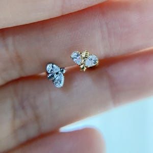 May include: Two small bee-shaped earrings. One is silver-toned with clear, teardrop-shaped stones. The other is gold-toned with clear, teardrop-shaped stones and a textured body. The earrings are designed to be worn in the ear.