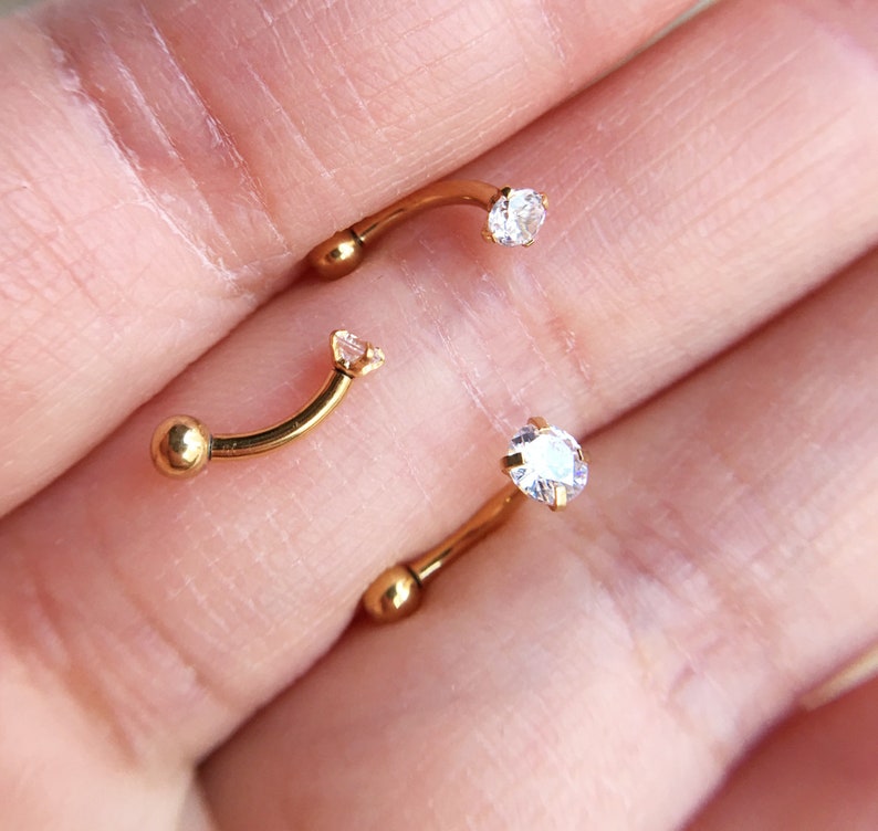Puede incluir: Tres piezas de joyer&iacute;a corporal de barra curva de color dorado con acentos de cristal transparente.