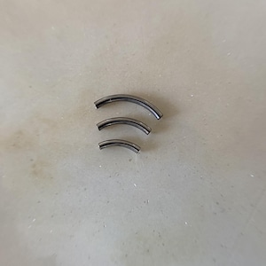 May include: Three curved, dark grey metal pieces of varying sizes. The pieces are arranged in a descending order, with the largest at the top and the smallest at the bottom. The objects are set against a light grey background.