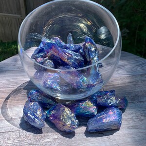 May include: A glass bowl filled with iridescent blue and purple crystals. The crystals are scattered around the bowl on a wooden surface.