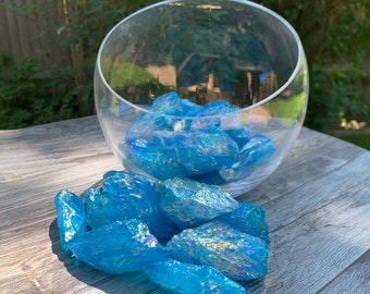 May include: A pile of iridescent blue quartz crystals on a wooden surface. The crystals are scattered around a clear glass bowl.