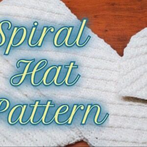 May include: A white crocheted hat and scarf set with a spiral stitch pattern. The set is laid out on a wooden surface. The text "Spiral Hat Pattern" is written in blue and yellow cursive on the scarf.