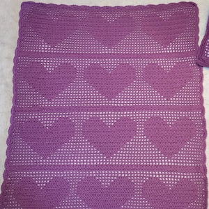 May include: A purple crocheted blanket with a geometric pattern. The blanket is made with a fine yarn and has a delicate, lacy look.