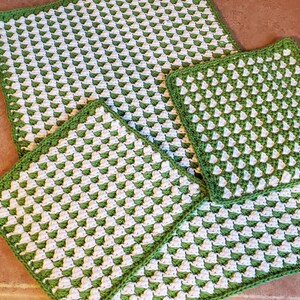 May include: Four crocheted dishcloths in a green and white pattern. The dishcloths are made with a textured stitch that creates a raised design.