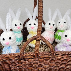 Könnte beinhalten: Ein Weidenkorb gefüllt mit sechs gehäkelten Osterhasen-Anhängern. Die Hasen sind weiß mit bunten Streifen und haben lange weiße Ohren.