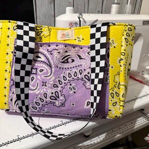 May include: A handmade tote bag with a yellow paisley pattern and a purple paisley pocket. The bag features black and white checkered straps and accents. A sewing machine is in the background.