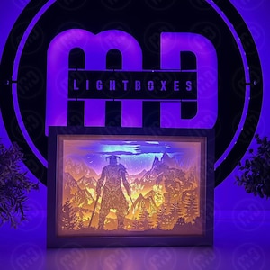 May include: A 3D layered paper light box with a white frame. The light box features a scene of a warrior in a forest with a blue sky and clouds. The light box is illuminated from behind, creating a shadow effect.