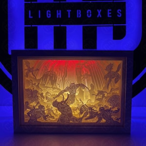 May include: A light-up 3D papercraft scene depicting a fantasy battle with a red and yellow color scheme. The scene features a large, imposing figure in the center, surrounded by smaller figures. The scene is framed in a black frame with the words "LIGHTBOXES" printed on the top.