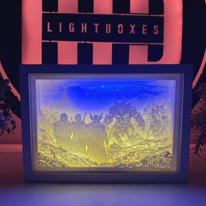 Könnte beinhalten: Eine beleuchtete Leuchtbox mit einer Fantasy-Szene. Das Kunstwerk zeigt Figuren, die einem großen Monster unter einem Sternenhimmel gegenüberstehen. Der Rahmen ist weiß, und der Hintergrund zeigt das Wort "LIGHTBOXES".
