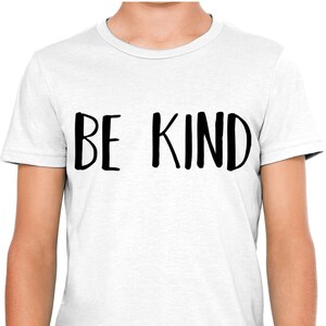 以下が含まれることがあります： 白いTシャツに黒い文字で「BE KIND」と手書きで書かれています。
